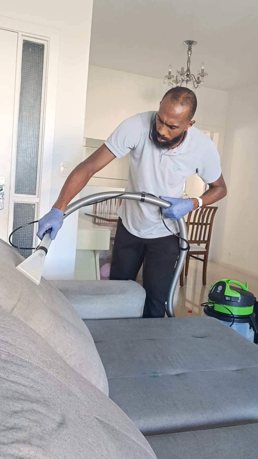 Profissional higienizando sofá cinza; atendimento da Ms Clean na Pituba, Salvador